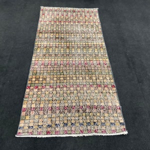 Puede incluir: Una alfombra vintage con un patrón geométrico en tonos marrones, beige, rojos y verdes. La alfombra tiene un aspecto desgastado y está hecha de lana.