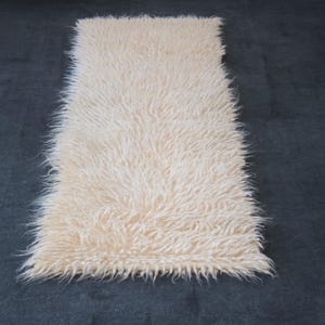 May include: A long, white faux fur rug with a soft, fluffy texture. The rug is perfect for adding a touch of luxury to any room.