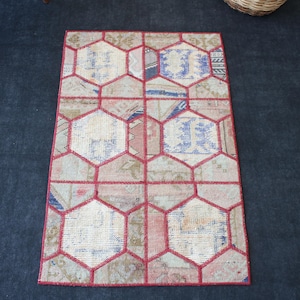 May include: A rectangular area rug featuring a patchwork design of muted beige, blue, and pink fabric segments. The rug is divided by a bold, red geometric grid pattern that forms a series of connected hexagons across the entire surface area.