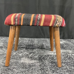 May include: A small wooden stool with four legs and a red, black and yellow striped fabric seat.