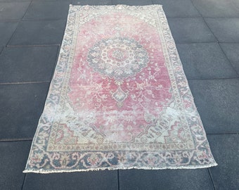 May include: A vintage pink and cream rug with a floral pattern and a dark gray border. The rug has a distressed look and is made of wool.