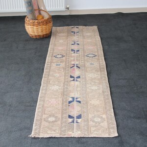 Könnte beinhalten: Ein langer, schmaler beigefarbener Läufer mit einem sich wiederholenden Muster aus blauen und rosa Blumenmotiven. Der Läufer hat einen Fransenrand.