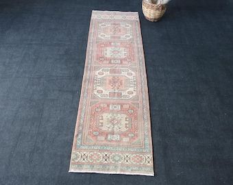 May include: A rectangular, vintage-style runner rug with a repeating geometric pattern in shades of red, beige, and green. The rug has a distressed look, with a central design and border details. The rug's dimensions are approximately 3 feet wide.