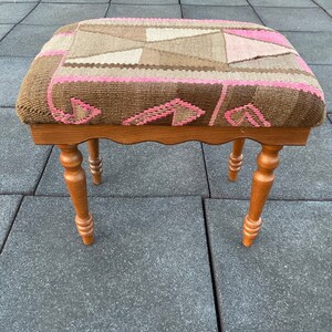 May include: A small wooden stool with turned legs and a woven tapestry seat featuring a geometric pattern in shades of brown and pink.