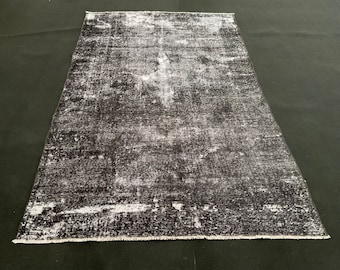 May include: A distressed black and white rug with a faded, vintage look. The rug has a subtle pattern and a frayed edge.