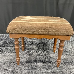 May include: A brown wooden stool with a woven fabric seat. The stool has turned legs and a scalloped edge.