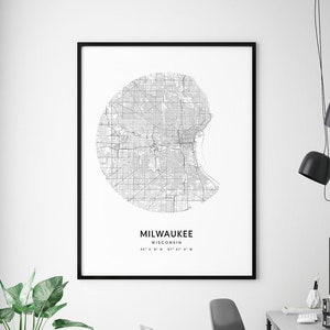 May include: Black and white map print of Milwaukee, Wisconsin with the city name and coordinates. The print is framed in a black frame and hanging on a white wall. The print is in a modern office setting with a desk, chairs, and computers.
