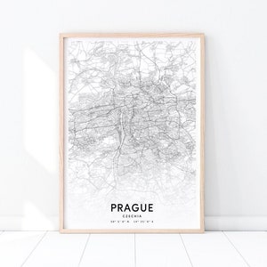 May include: A framed black and white map print of Prague, Czechia. The map details the city's streets and waterways. The print is in a light wood frame and includes the city name and coordinates.