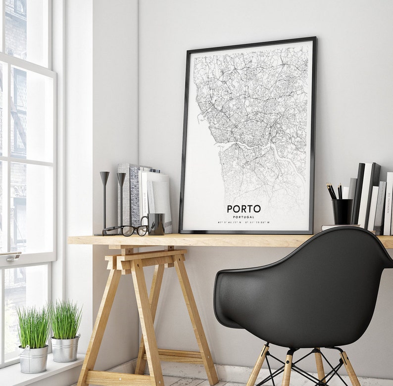 May include: A black and white map print of Porto, Portugal, framed in a black frame, hangs above a wooden desk with a black chair. The desk has a wooden easel and a pair of glasses on top.
