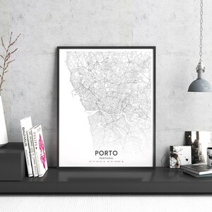 May include: Black and white map print of Porto, Portugal in a black frame. The map shows the city streets and includes the coordinates 41&deg;09'43.71" N 8&deg;37'18.05" W. The print is on a shelf with books and other decor.