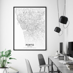 May include: Black and white map print of Porto, Portugal, in a black frame hanging on a white wall. The map shows the city streets and waterways. The print is hanging above a gray desk with two chairs and a computer monitor.