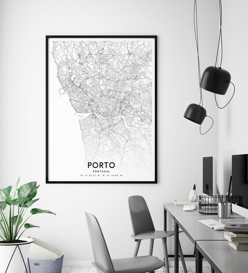 May include: Black and white map print of Porto, Portugal, in a black frame hanging on a white wall. The map shows the city streets and waterways. The print is hanging above a gray desk with two chairs and a computer monitor.