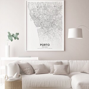 May include: A black and white map print of Porto, Portugal, with the city name and coordinates printed at the bottom. The map is framed and hanging on a white wall above a white couch with beige pillows.
