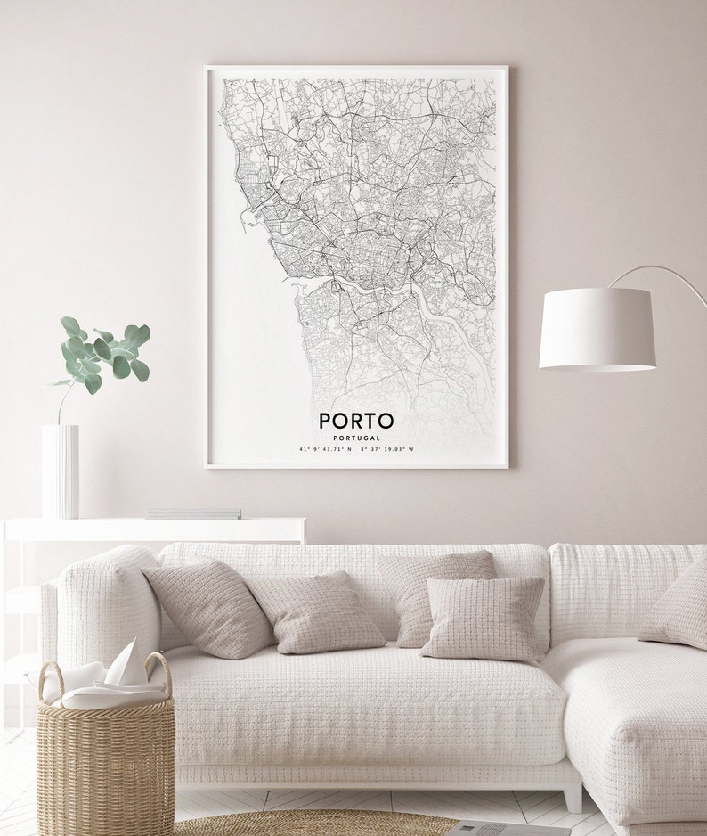 May include: A black and white map print of Porto, Portugal, with the city name and coordinates printed at the bottom. The map is framed and hanging on a white wall above a white couch with beige pillows.