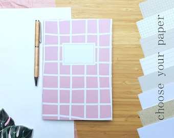 Könnte beinhalten: Ein rosa-weiß kariertes Notizbuch mit leerem Etikett, ein Holzstift und verschiedene Papierproben. Die Worte "choose your paper" sind vertikal auf der rechten Seite aufgedruckt. Die Artikel sind auf einer Bambusoberfläche angeordnet.
