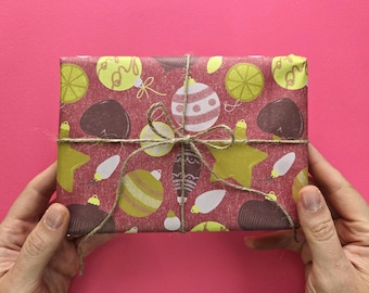 Könnte beinhalten: Ein rechteckiges Geschenkpaket, eingewickelt in kastanienbraunes Papier mit einem wiederkehrenden Muster aus gelben, weißen und dunkelbraunen Weihnachtskugeln und Sternen. Das Paket ist mit einer dünnen, naturfarbenen Paketschnur umwickelt.