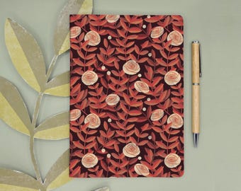 Könnte beinhalten: Ein rechteckiges Notizbuch mit dunkelbraunem Hintergrund und einem sich wiederholenden Muster aus hellpfirsichfarbenen Rosen und rotbraunen Blättern, begleitet von einem hellen Holzkugelschreiber, der vertikal rechts neben dem Notizbuch liegt.