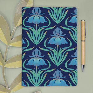 Pode incluir: Um caderno retangular com um padrão repetitivo de flores de íris azuis com caules e folhas verde-claras sobre um fundo azul-marinho escuro, acompanhado por uma caneta esferográfica de madeira clara com detalhes em metal prateado.