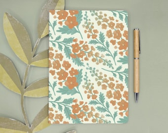Könnte beinhalten: Ein rechteckiges Notizbuch mit einem sich wiederholenden Blumenmuster aus orangefarbenen Blüten und salbeigrünen Blättern auf cremefarbenem Grund, begleitet von einem hellen Holzkugelschreiber mit silbernem Clip und Spitze, vertikal ausgerichtet.