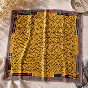 May include: A square scarf featuring a vibrant yellow center with a repeating pattern of small brown stirrups. The border is a dark brown frame with a striped design in red, white, and green, accented by white line drawings of horse bits.