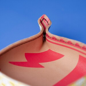 May include: Close-up of the inside of a small, beige leather tray with a red lightning bolt design. The tray has a stitched edge and is folded in half.