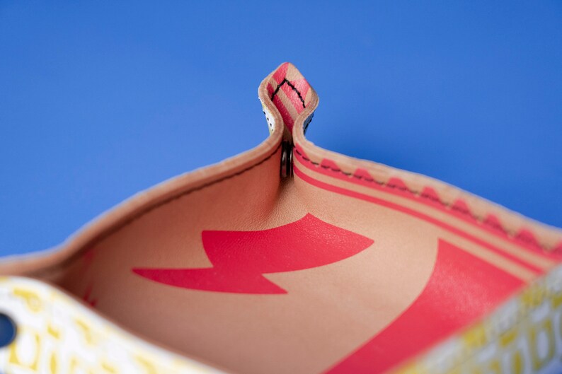 May include: Close-up of the inside of a small, beige leather tray with a red lightning bolt design. The tray has a stitched edge and is folded in half.