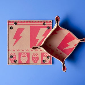 May include: Two brown leather trays with red lightning bolt and owl designs. The trays are folded open and the inside of the trays are visible. The trays are on a blue background.