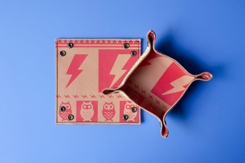 May include: Two brown leather trays with red lightning bolt and owl designs. The trays are folded open and the inside of the trays are visible. The trays are on a blue background.