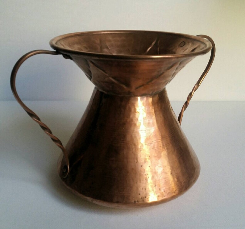 May include: A hammered copper vase with two twisted wire handles. The vase has a wide, flared top and a narrow base.