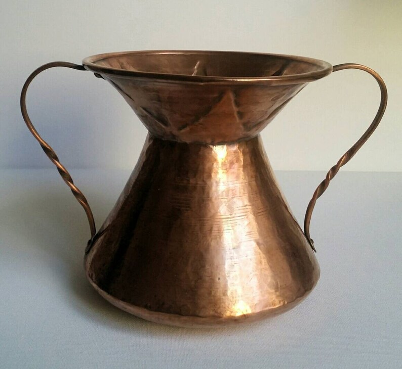 May include: A hammered copper vase with two twisted wire handles. The vase has a wide mouth and a narrow base.