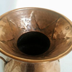 May include: A hammered copper vase with a wide mouth and two handles. The vase has a rustic, antique look.