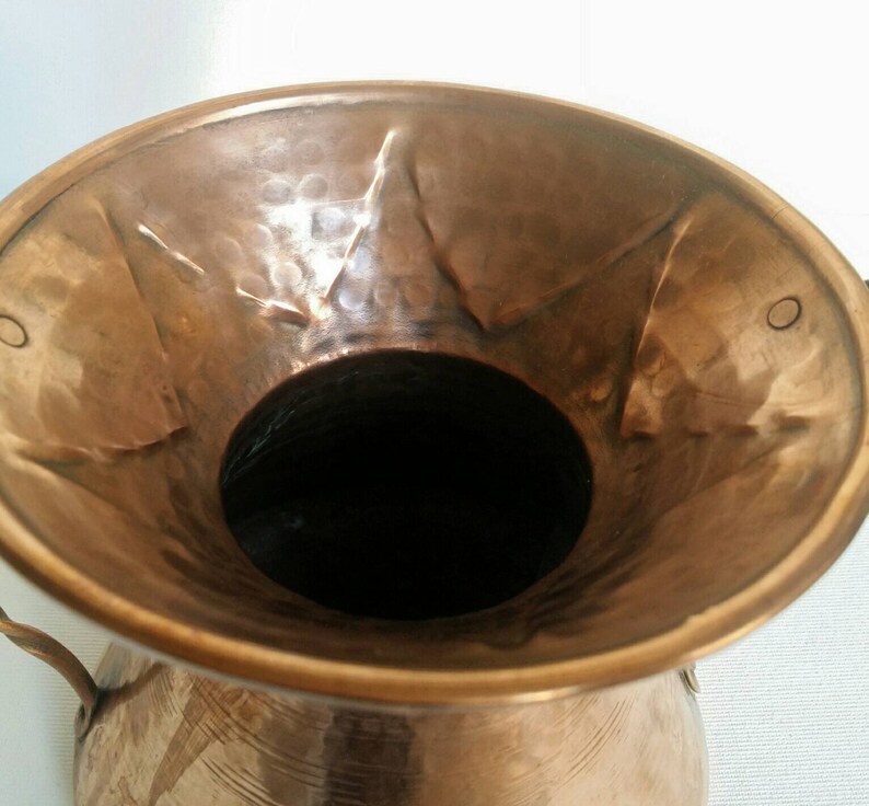 May include: A hammered copper vase with a wide mouth and two handles. The vase has a rustic, antique look.