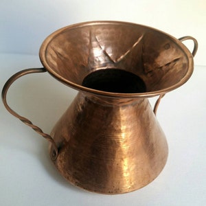 May include: A hammered copper vase with two twisted handles. The vase has a wide, flared opening and a rounded, conical body.