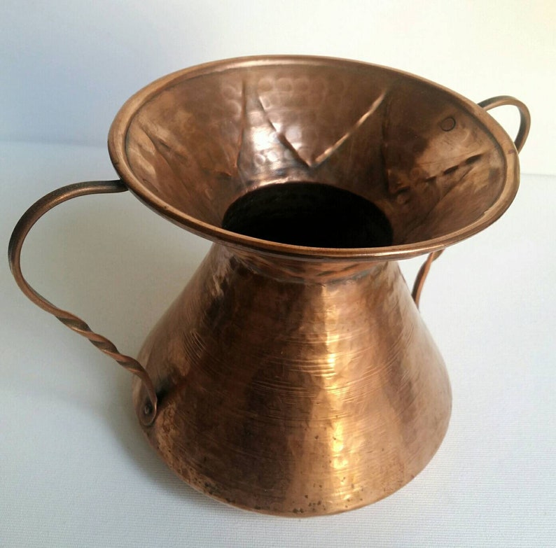 May include: A hammered copper vase with two twisted handles. The vase has a wide, flared opening and a rounded, conical body.