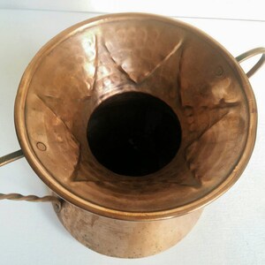 May include: A hammered copper planter with two twisted wire handles. The planter has a wide, flared opening and a rounded bottom.