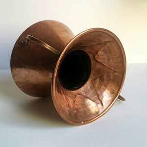 May include: A hammered copper vase with two handles. The vase is a deep copper color and has a hammered texture. The vase is empty and ready to be filled with flowers.