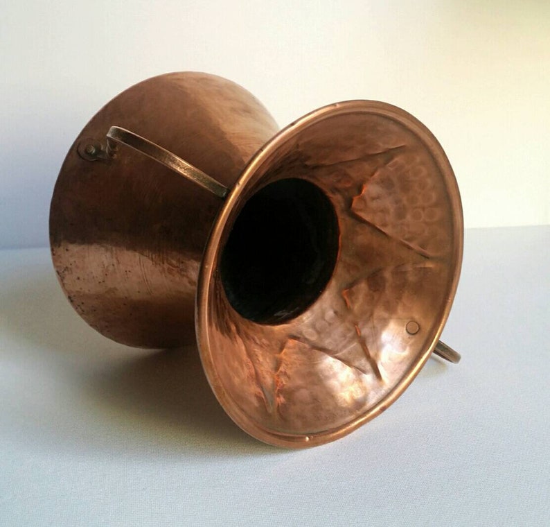 May include: A hammered copper vase with two handles. The vase is a deep copper color and has a hammered texture. The vase is empty and ready to be filled with flowers.