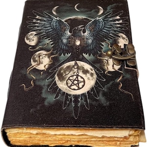 May include: A black leather journal featuring a raven design with moons and a pentagram. The journal has a metal clasp and aged paper pages. The cover is dark with a detailed illustration.