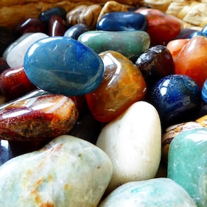 Pode incluir: Uma coleção de pedras lisas e polidas em várias cores, incluindo azul, verde, vermelho, laranja e branco. As pedras estão dispostas em uma cesta, criando uma exibição visualmente atraente.