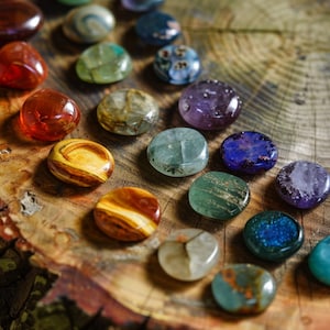 May include: A collection of smooth, polished stones in various colors, arranged in a rainbow pattern on a wooden surface. The stones are likely used for healing or meditation.
