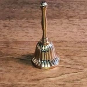 Op de afbeelding: Een kleine, gouden bel met een geribbeld ontwerp en een lange steel.