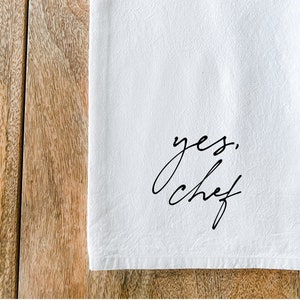 May include: White kitchen towel with black cursive text that reads "yes, chef".