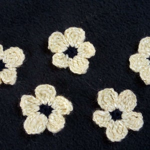 May include: Five crocheted white flowers with black centers on a black background.