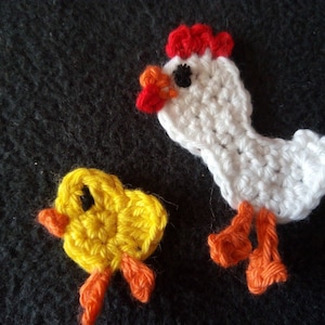 Könnte beinhalten: Ein weißes gehäkeltes Huhn mit rotem Kamm und orangefarbenen Füßen, neben einem gelben gehäkelten Küken mit orangefarbenen Füßen.