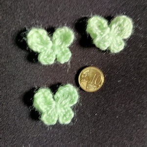 Può includere: Tre decorazioni a forma di farfalla in crochet verde, ciascuna delle dimensioni di una moneta da 10 centesimi di euro.