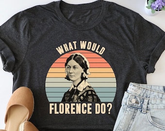 May include: A dark gray t-shirt with a vintage-style graphic of Florence Nightingale. The graphic features a sunset background with the text "What Would Florence Do?"