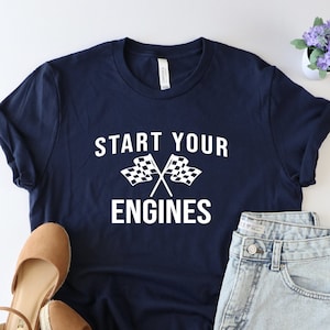 May include: A navy blue t-shirt with the text "Start Your Engines" in white lettering. The shirt features a pair of crossed checkered flags in white.
