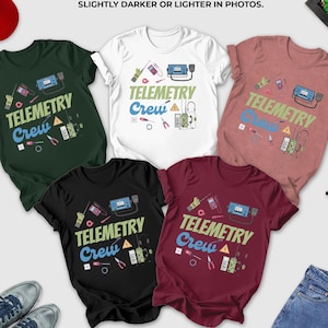 May include: T-shirts in forest green, white, heather mauve, black, and maroon, each with the text "Telemetry Crew" and related graphics. A red baseball cap, sunglasses, and jeans are also visible.