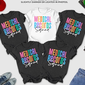 May include: A collection of t-shirts in dark grey heather and white, featuring the text "MEDICAL RECORDS Squad" in colorful block letters. A red baseball cap, sunglasses, and jeans are also visible.