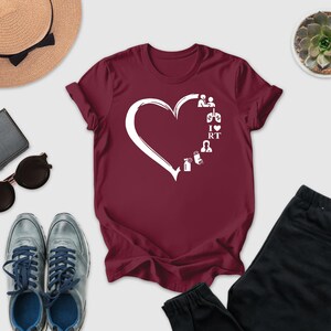 a casual outfit consisting of a burgundy t-shirt with a white heart design, a pair of gray sneakers, a pair of black pants, sunglasses, a hat, and a small potted succulent plant.